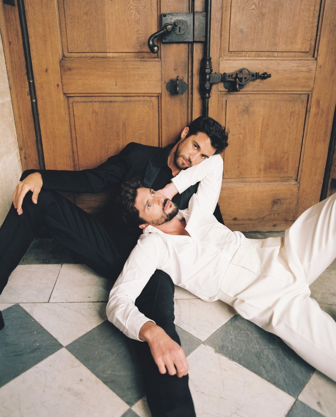 Two grooms resting against an old wooden door